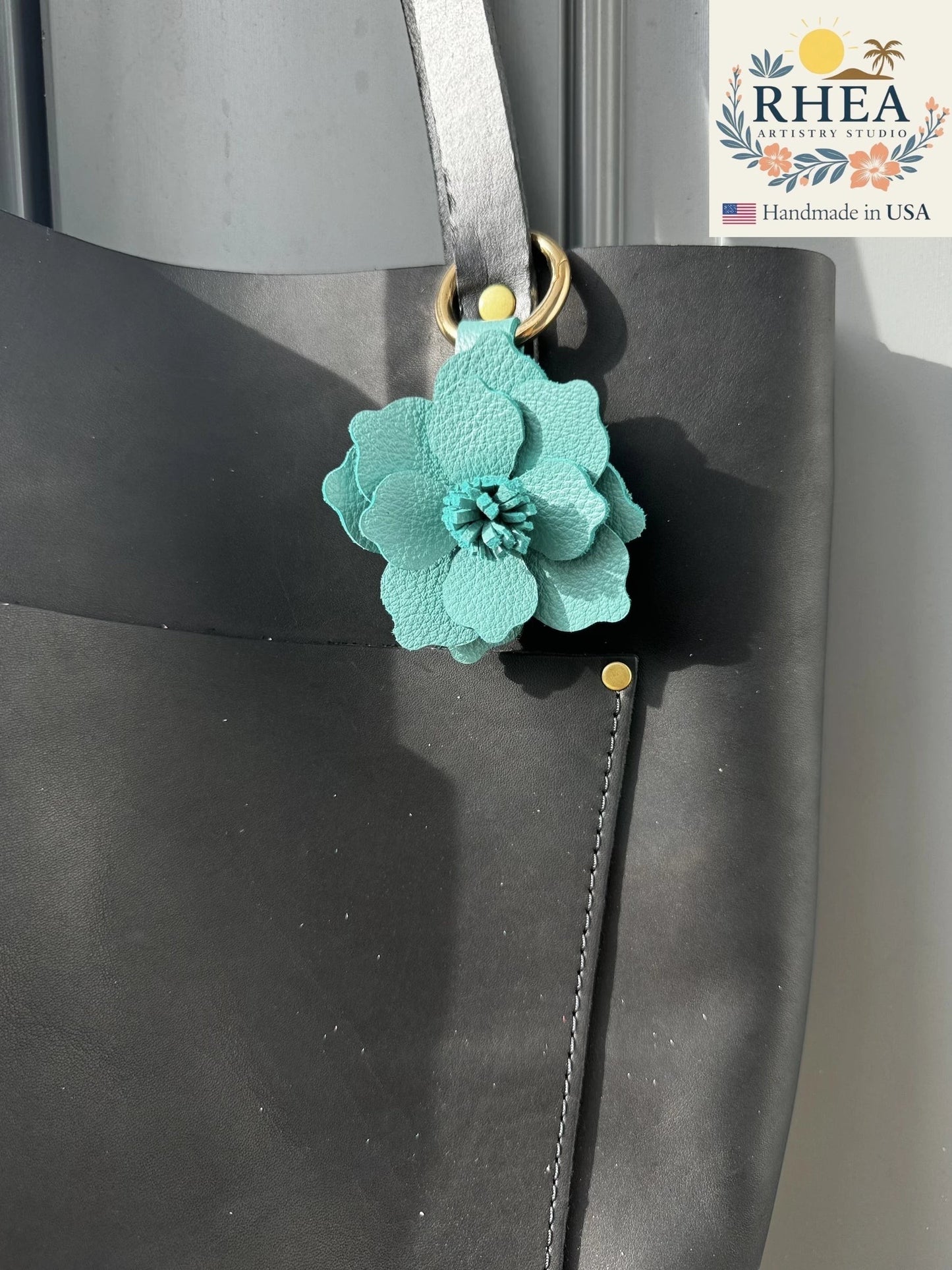 Rhea Artistry Studio teal leather flower charm with lobster clasp and split ring attached to a black tote bag.