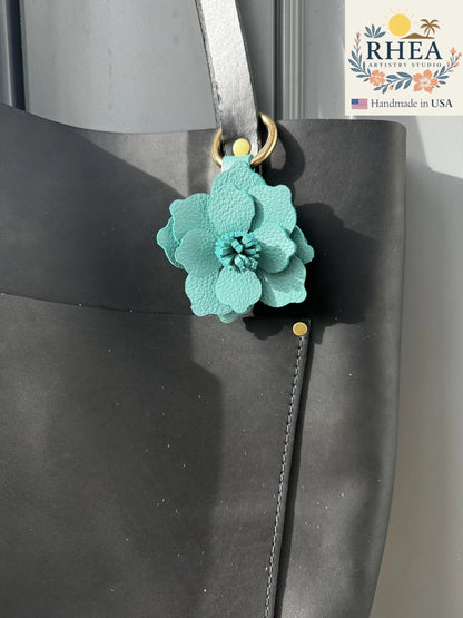 Rhea Artistry Studio teal leather flower charm with lobster clasp and split ring attached to a black tote bag.