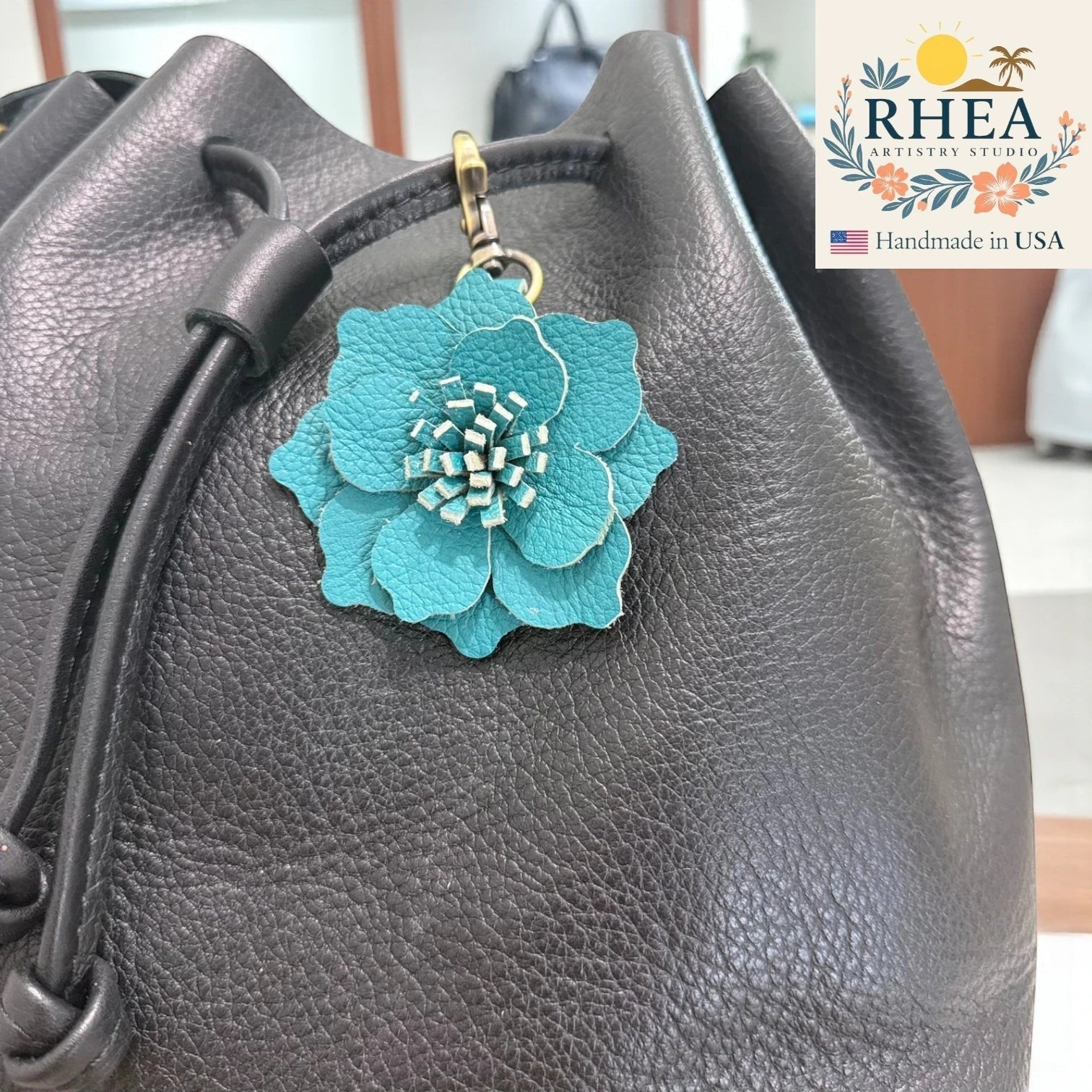 Rhea Artistry Studio teal leather flower charm attached to a black leather handbag. Handcrafted floral accessory.