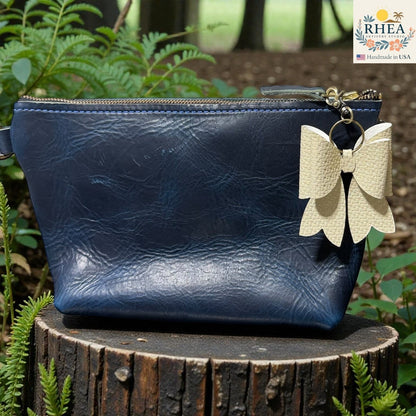 Rhea Artistry Studio textured double-layer French bow bag charm in cream, attached to a navy blue leather pouch.