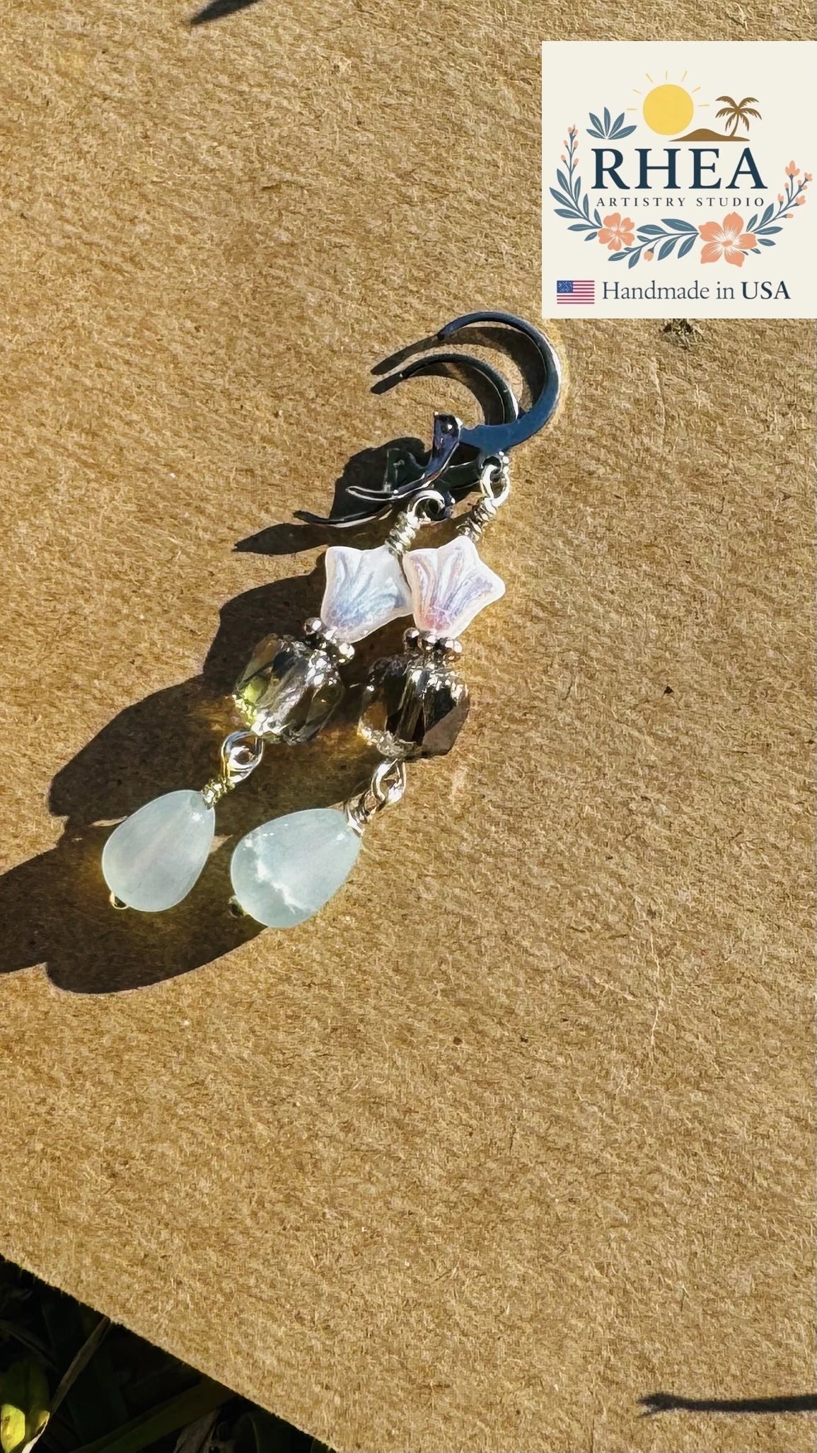 Rhea Artistry Studio white and silver three petal cathedral drop earrings with blue gemstone drops and French lever back closure.