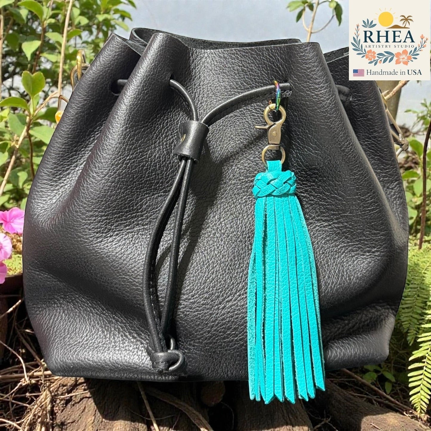 Rhea Artistry Studio turquoise leather tassel bag charm with braided detail and brass clasp on a black leather drawstring bag.
