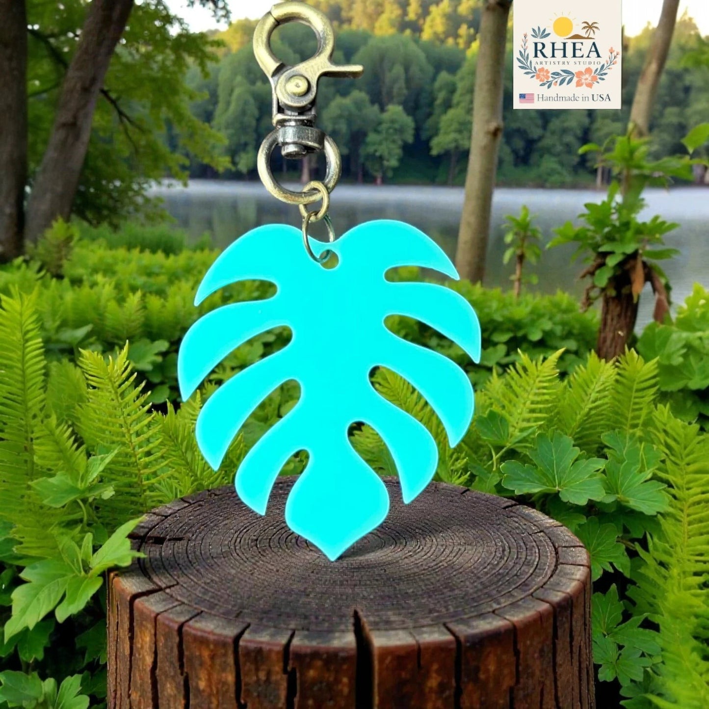 Rhea Artistry Studio turquoise monstera leaf acrylic charm with antique brass clasp, displayed on a wooden stump.