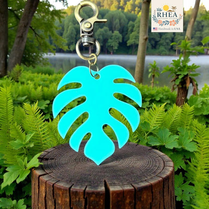 Rhea Artistry Studio turquoise monstera leaf acrylic charm with antique brass clasp, displayed on a wooden stump.