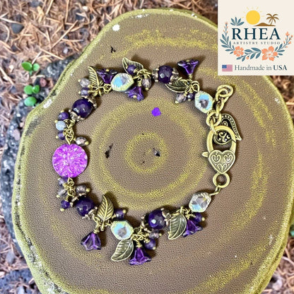 Rhea Artistry Studio violet glass bead bracelet with antique brass leaf accents and heart clasp. Features floral charms and natural gemstones.