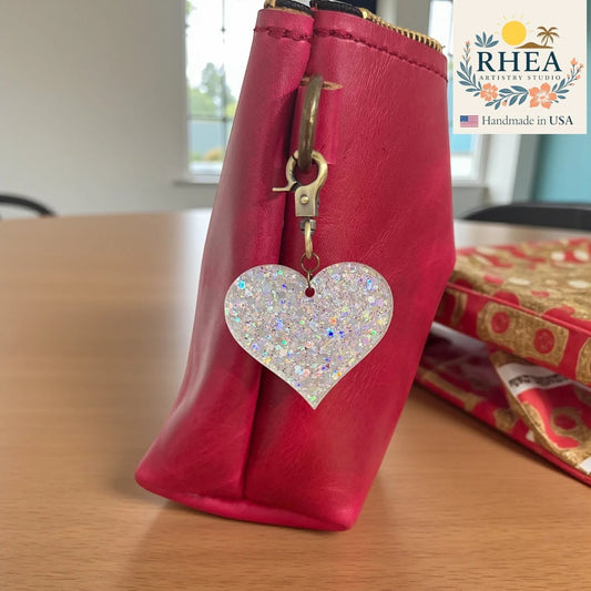 Rhea Artistry Studio white glitter heart charm with antique brass clasp on a pink bag.