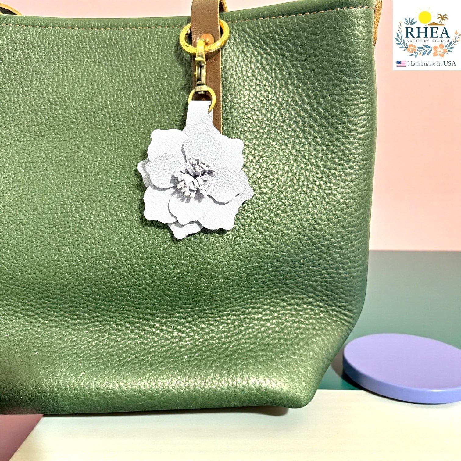 Rhea Artistry Studio white leather flower charm attached to a green pebbled leather tote bag.