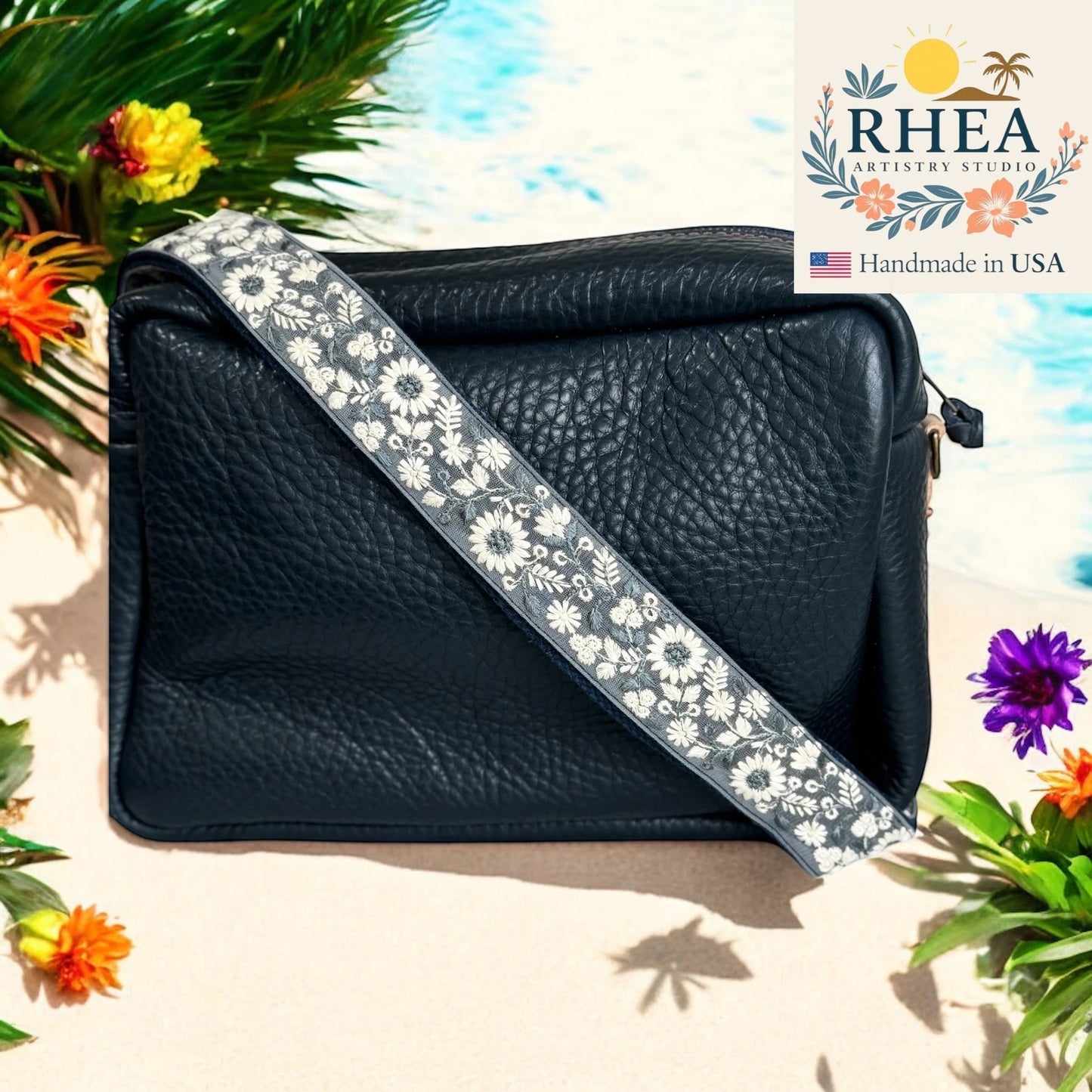 Rhea Artistry Studio navy crossbody bag with a 1.5-inch adjustable strap featuring white wildflower embroidery and brushed brass hardware.