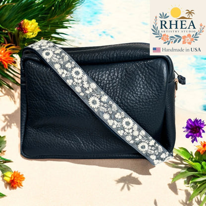 Rhea Artistry Studio navy crossbody bag with a 1.5-inch adjustable strap featuring white wildflower embroidery and brushed brass hardware.