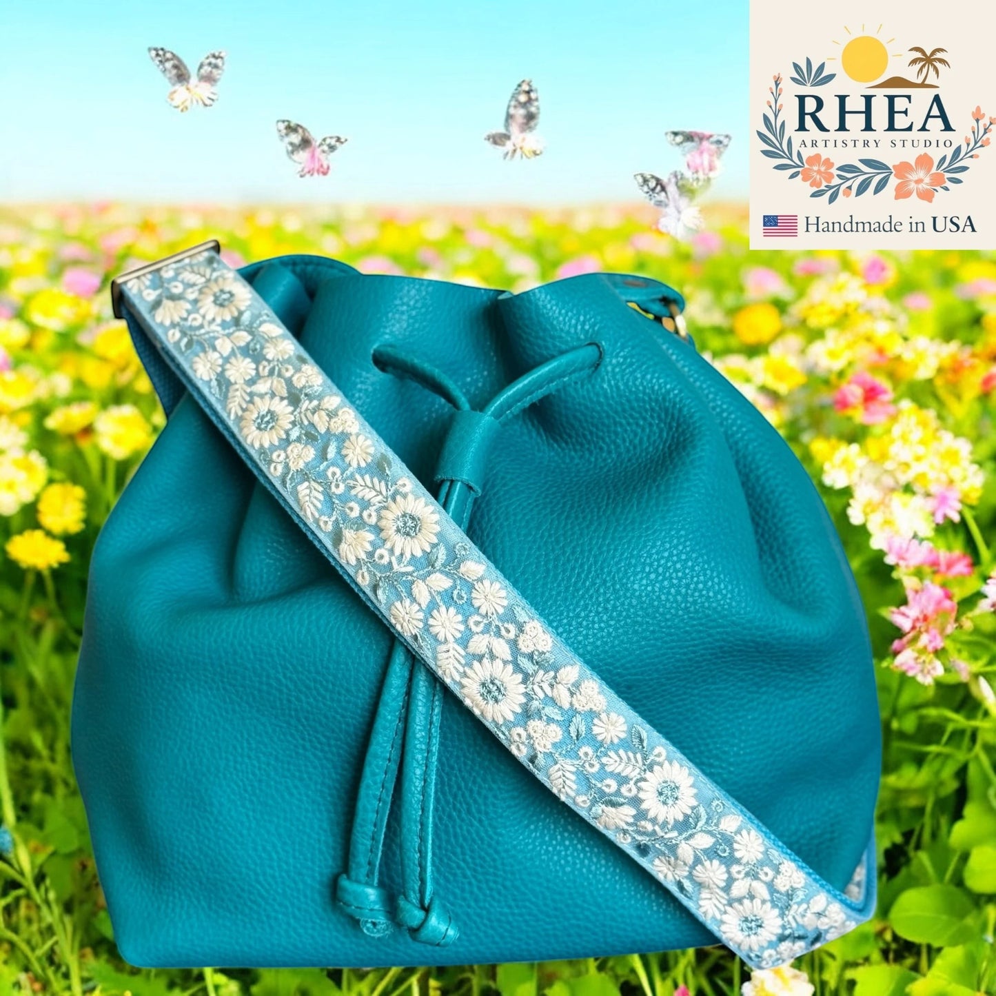 Rhea Artistry Studio teal leather bucket bag with a 1.5-inch adjustable crossbody strap featuring white wildflower embroidery and brushed brass hardware.