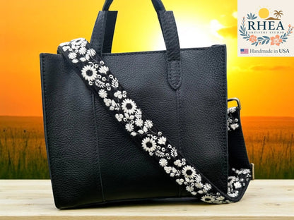 Rhea Artistry Studio black crossbody strap with white embroidered wildflowers, 1.5-inch wide, adjustable length.