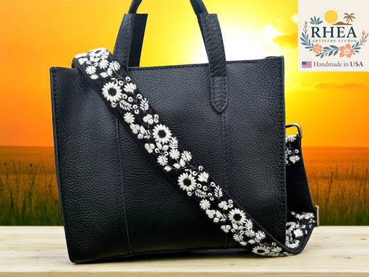 Rhea Artistry Studio black crossbody strap with white embroidered wildflowers, 1.5-inch wide, adjustable length.