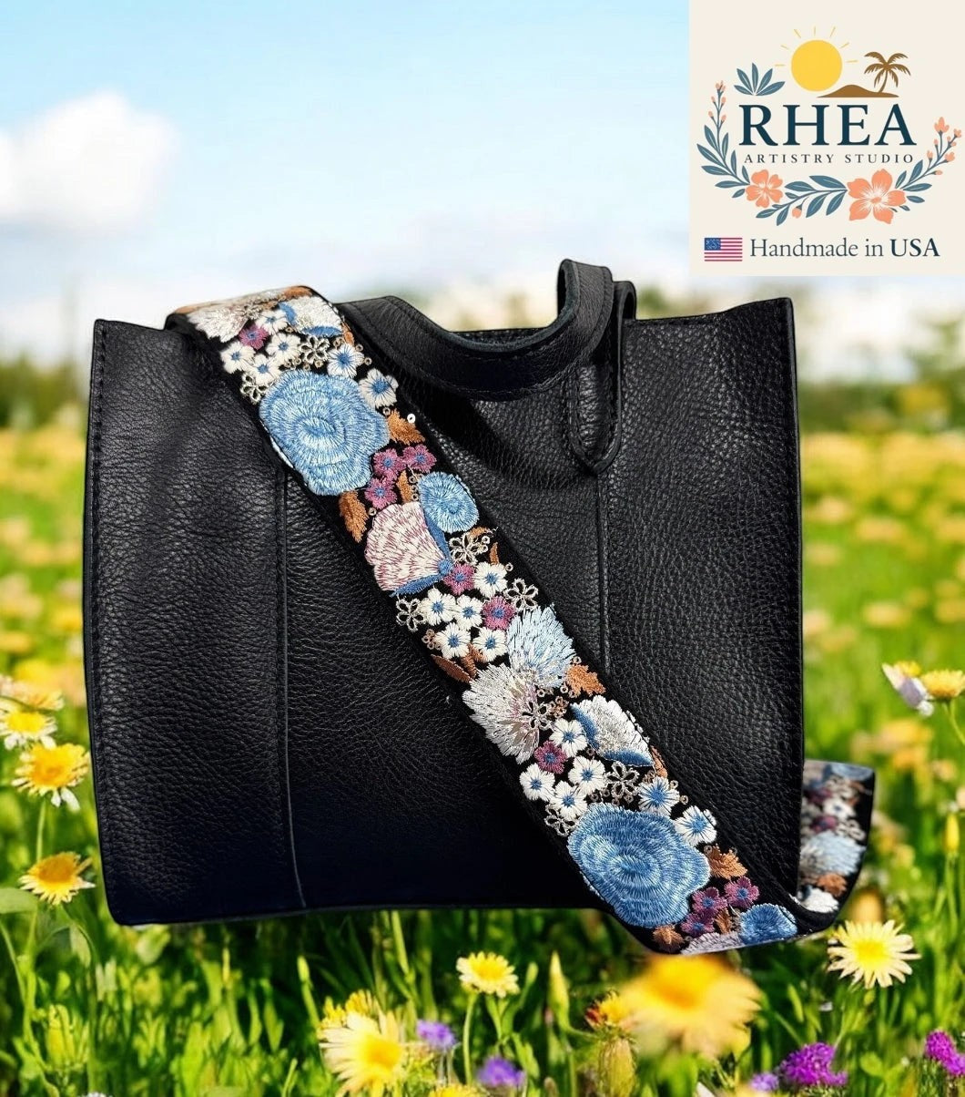 Rhea Artistry Studio black crossbody strap with blue, white, and pink wildflower embroidery, 2-inch width, adjustable length.