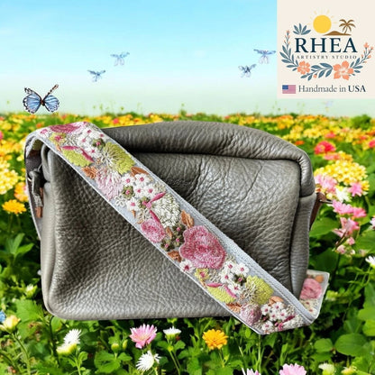 Rhea Artistry Studio grey leather crossbody bag with a 2-inch wide wildflower embroidered strap in pink, white, and green.