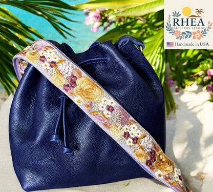 Rhea Artistry Studio navy blue leather bucket bag with a 2-inch wide wildflower embroidered strap in purple, gold, and white.