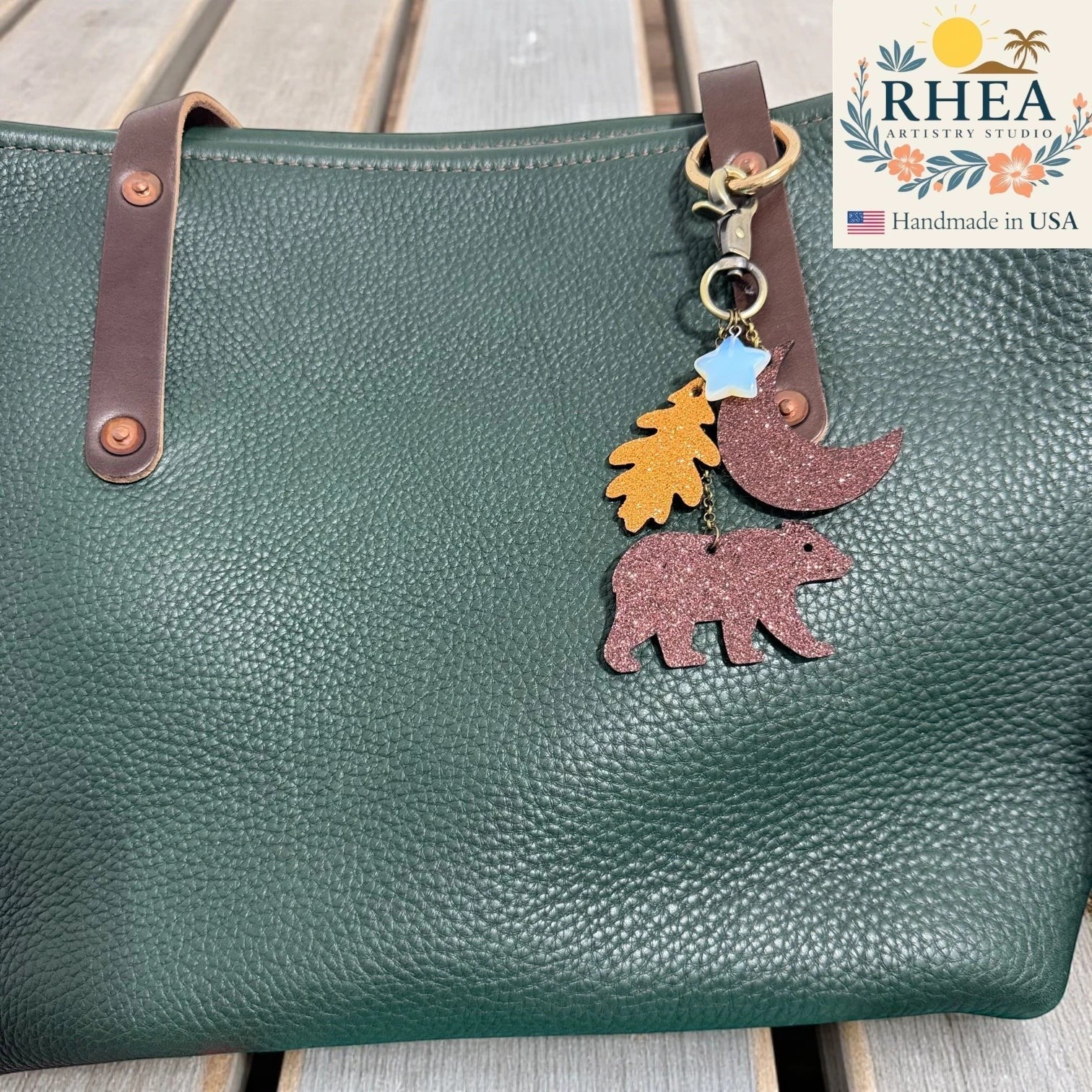 Rhea Artistry Studio woodland whimsy leather keychain charm with bear, leaf, moon, and star charms on a green pebbled leather tote bag.