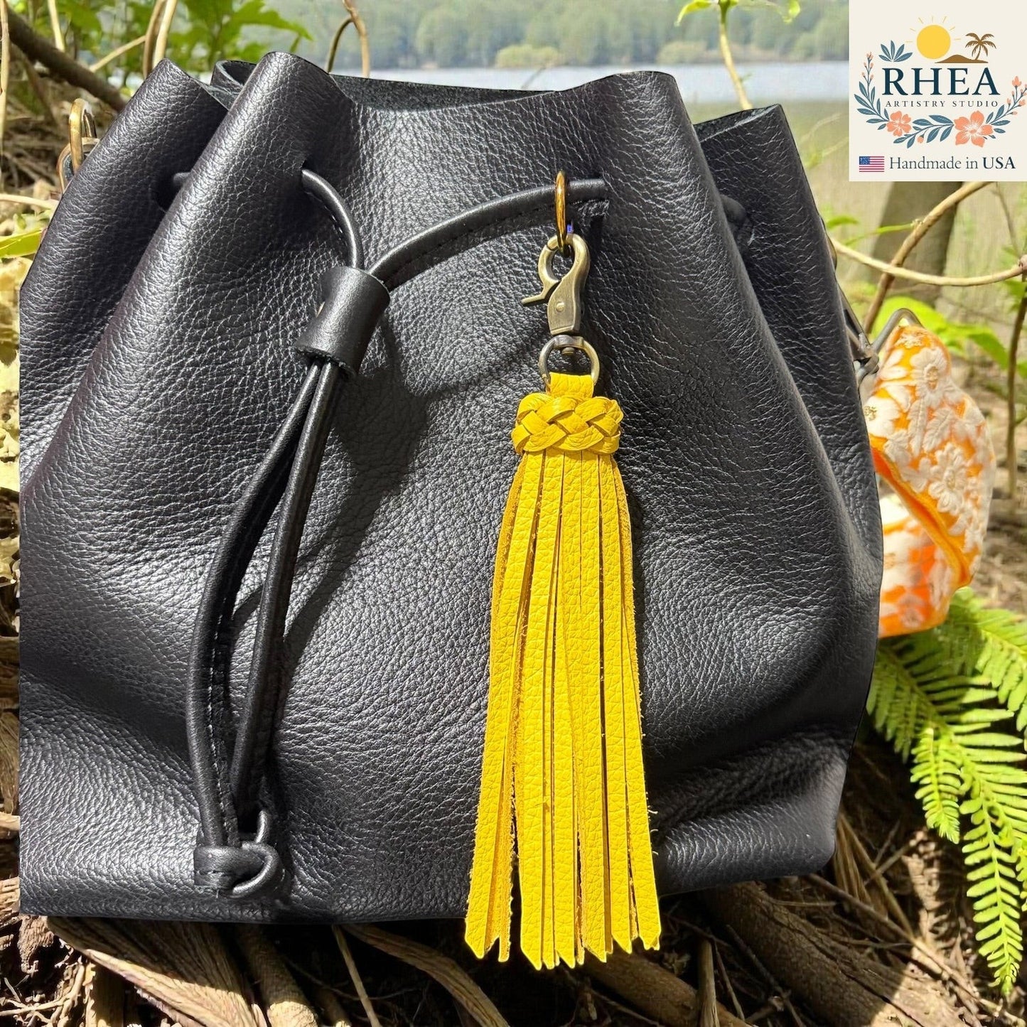 Rhea Artistry Studio yellow leather tassel bag charm with braided detail and brass clasp on a black leather bag.