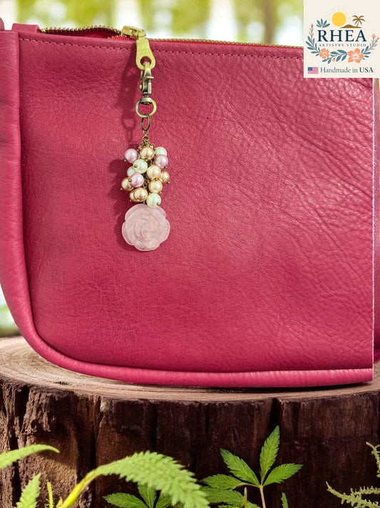 Pink leather pouch with a decorative keychain on a wooden surface with greenery.