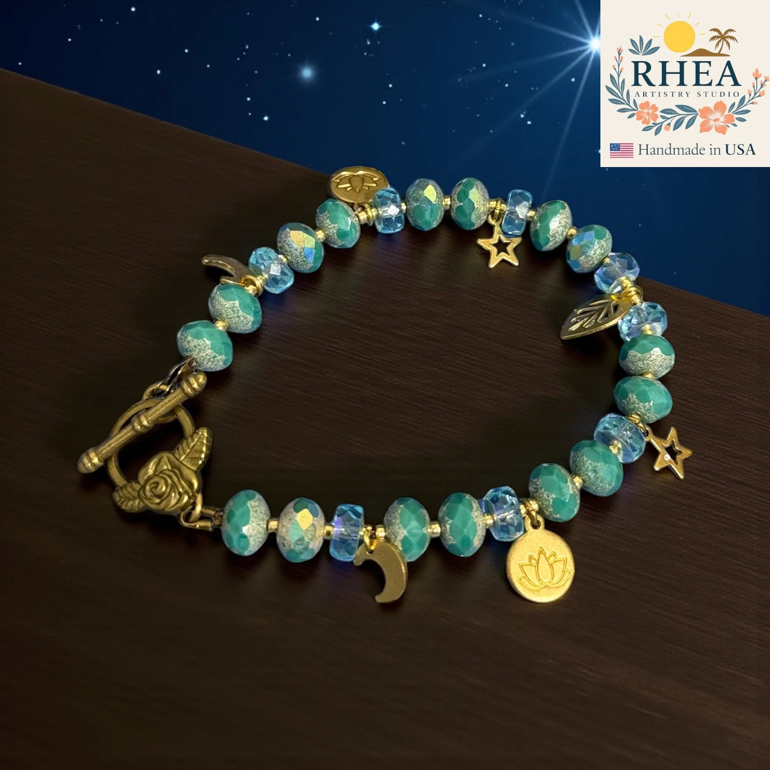 Turquoise beaded bracelet with gold charms on a dark surface, RHEEA Artistry Studio logo in the corner.