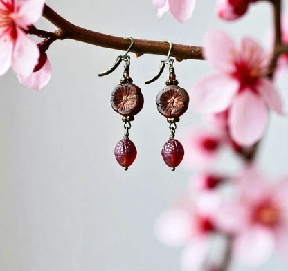 Earrings with red beads and gold accents hanging from a branch with pink flowers.