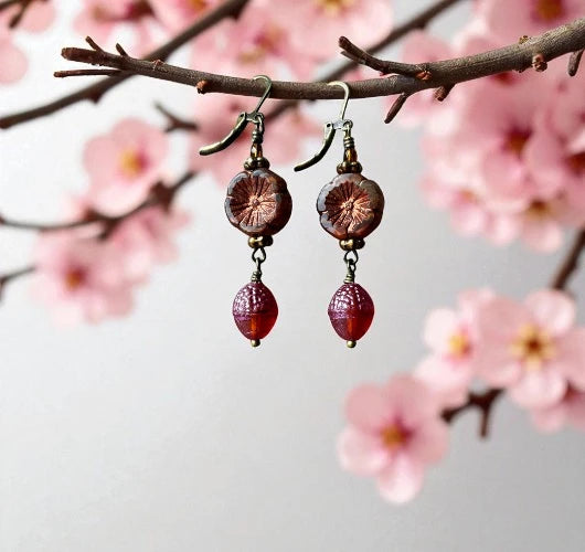 Pair of earrings with purple beads hanging from a branch with pink flowers.