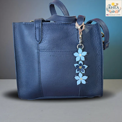 Blue leather handbag with a floral keychain charm on a gray surface