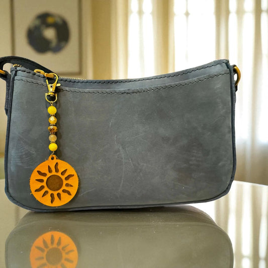Gray handbag with a sun-shaped charm on a reflective surface