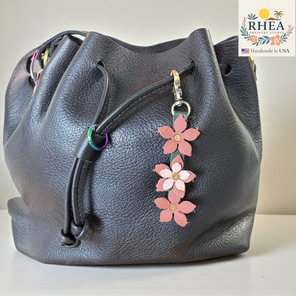 Handmade leather floral charm clipped to a handbag in  pinkish hues