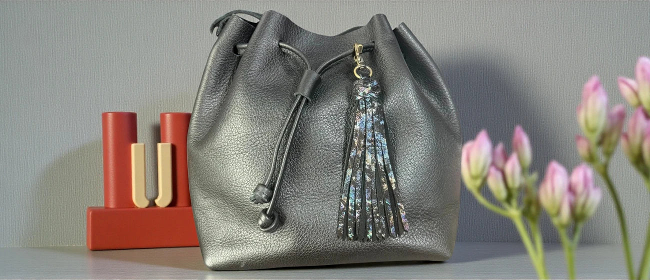 Silver drawstring bag with a tassel on a gray surface with pink flowers in the background