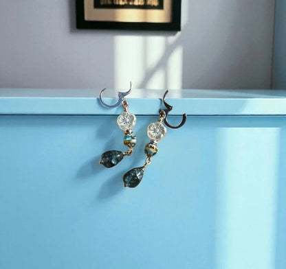 Pair of earrings with green teardrop-shaped stones on a light blue surface.