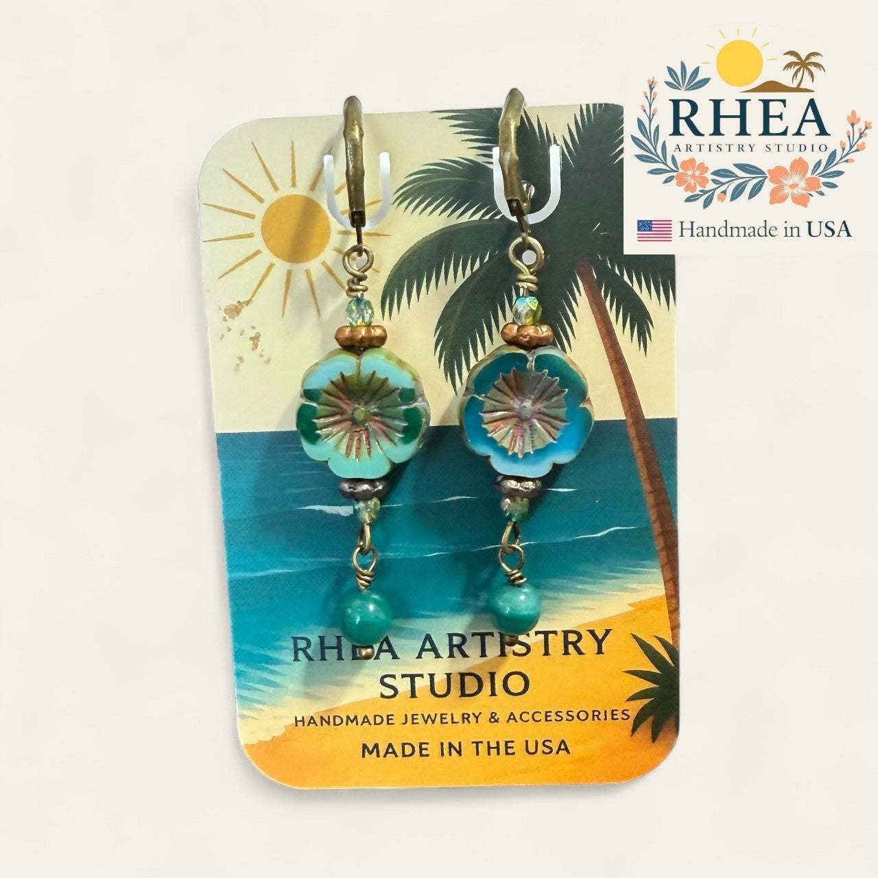 Tropical-themed earrings on a Rhea Artistry Studio card with palm tree and beach design.