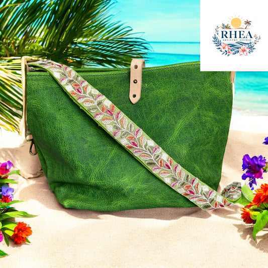 Colorful leaf-patterned strap in green, pink, and red tones on a green leather bag, photographed beachside