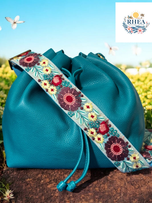 Soft blue embroidered bag strap featuring yellow and mauve floral patterns on a baja drawstring leather bag.