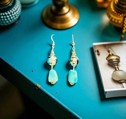 Turquoise beaded earrings on a teal surface with decorative items.
