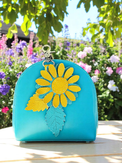 Mustard and Turquoise  leather daisy charm with brushed brass clasp in a garden setting