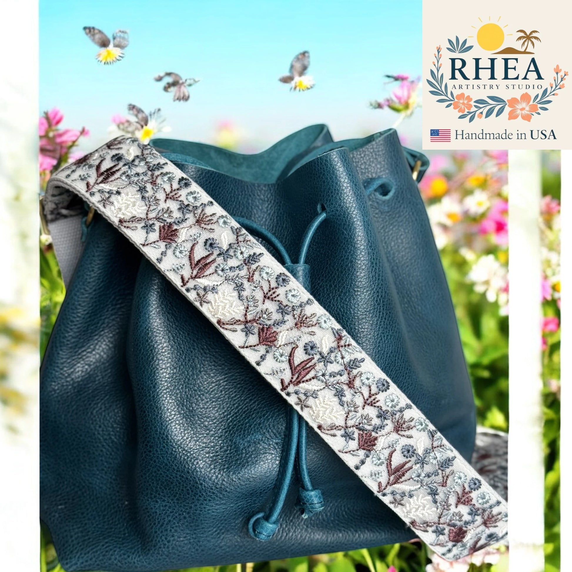 Blue leather bag with a floral purse strap against a floral background, featuring the Rhea Artistry Studio logo.