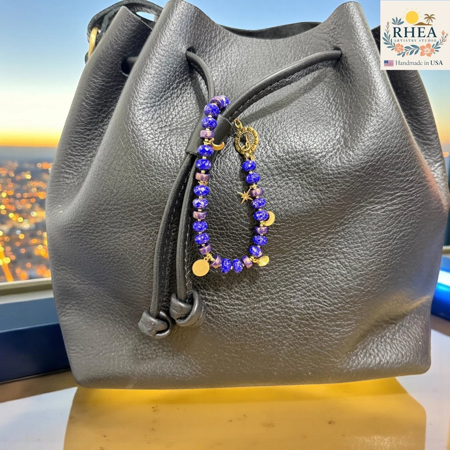 Gray leather handbag with a beaded charm against a cityscape background