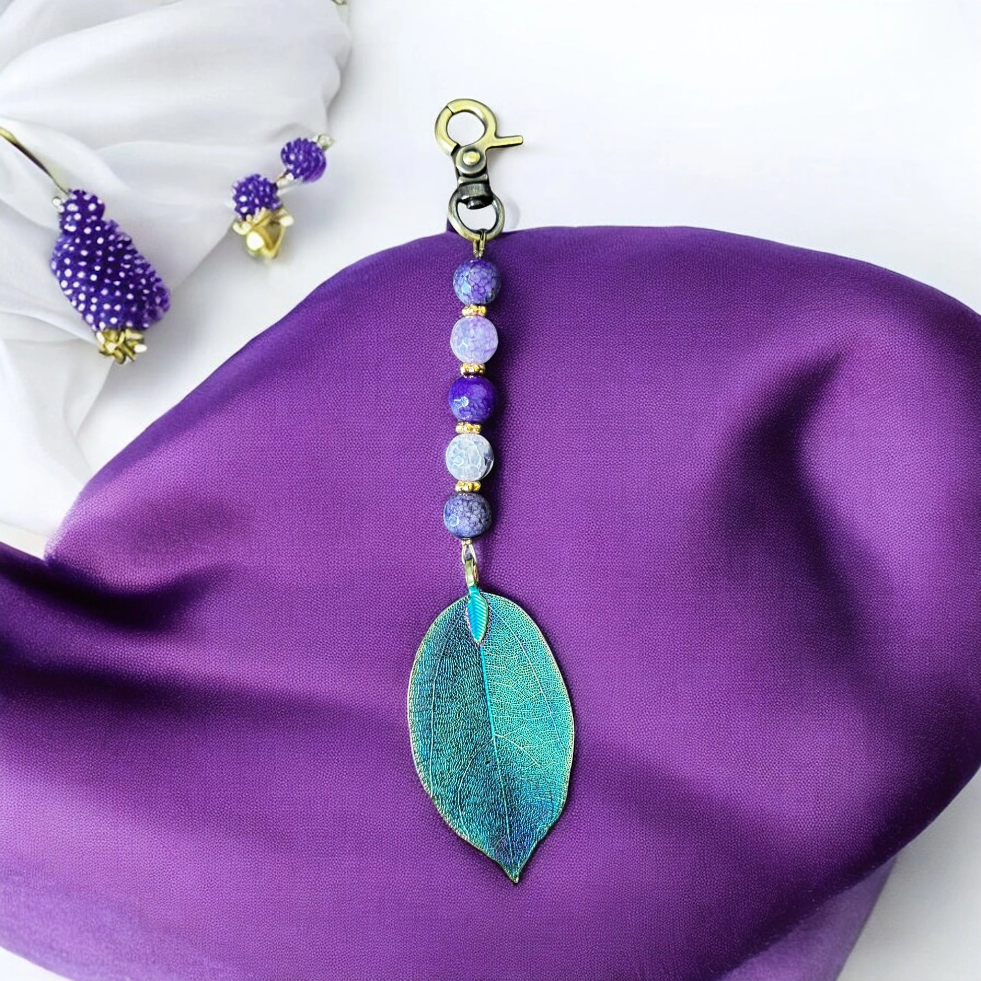 Violet gemstone bag charm with electroplated leaf pendant on white stone background