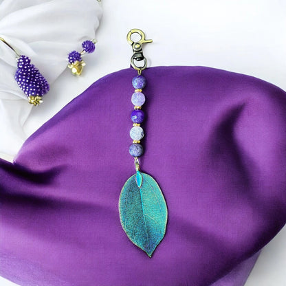 Violet gemstone bag charm with electroplated leaf pendant on white stone background