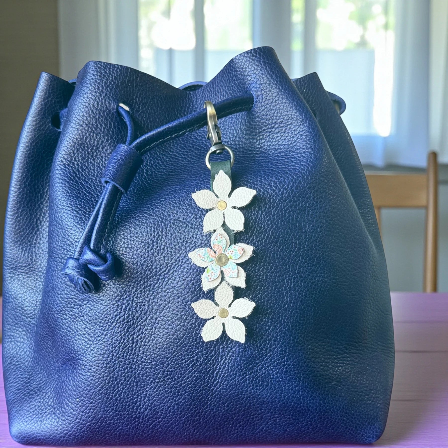 White floral-embossed leather charm with brushed brass clasp – elegant handcrafted detail.