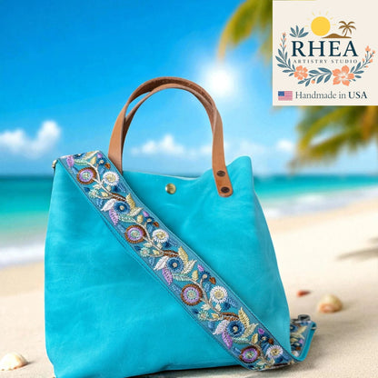 Turquoise handbag with a floral strap on a beach, featuring the RHEA Artistry Studio logo.