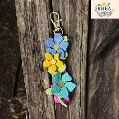 Colorful flower-shaped keychain on a wooden surface with RHEEA branding.