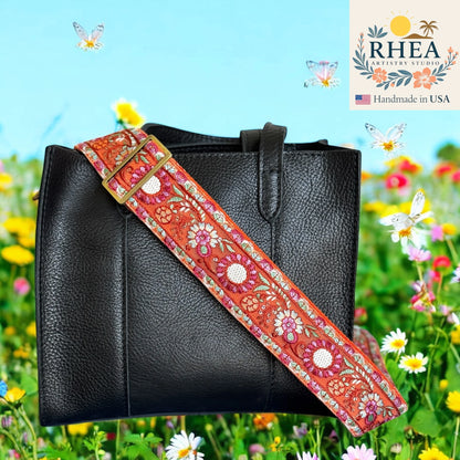 Black handbag with a colorful floral purse strap against a floral background, featuring the RHEA brand.